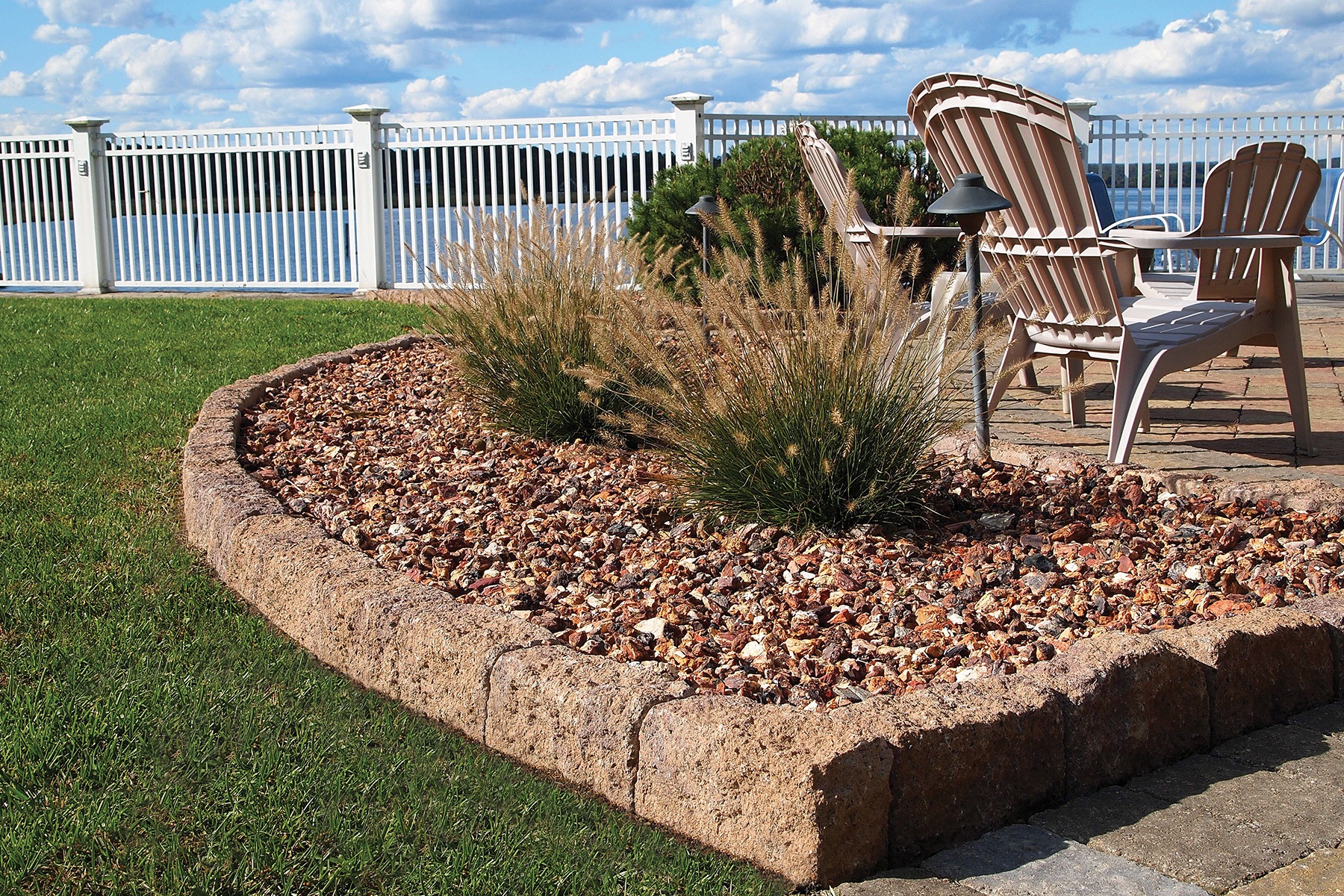 Curved row of smooth, gray edge stones for garden separating lush green grass from a flower bed with colorful blooms.