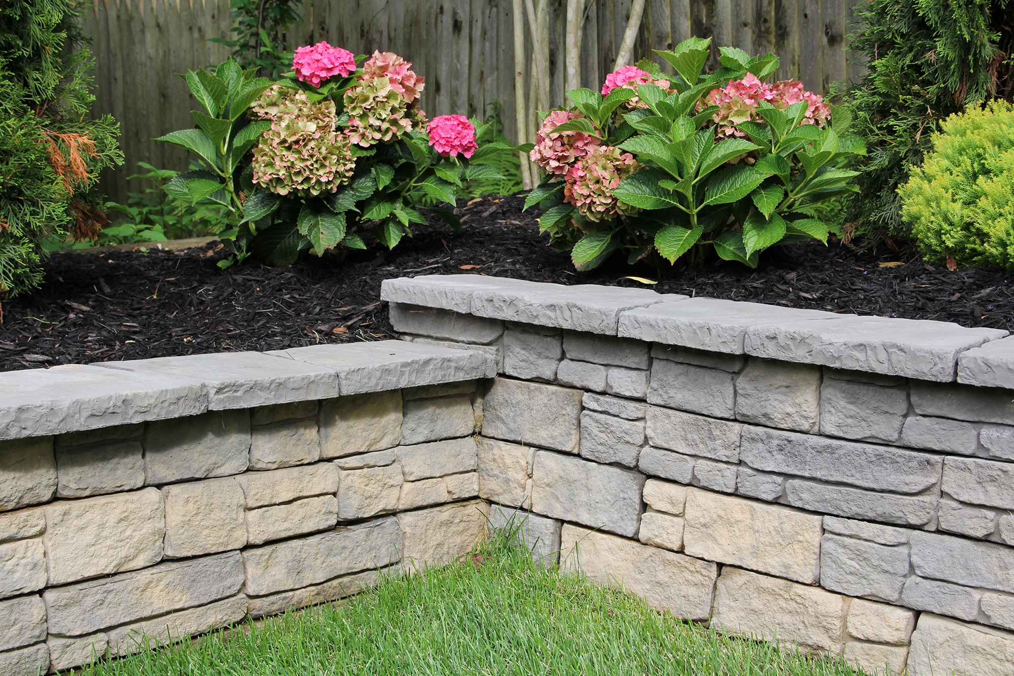 Tiered stone garden walls bordering fresh hydrangeas and evergreen shrubs above neatly trimmed grass.