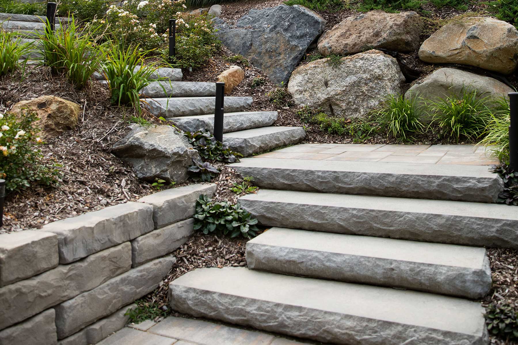 Natural gray granite steps stone arranged in a garden pathway surrounded by green grass and small plants.