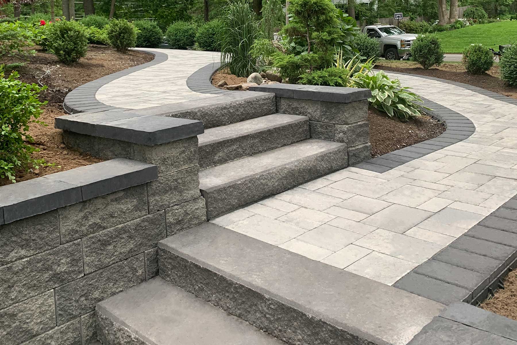 Rustic outdoor stone steps leading through a mossy garden path bordered by lush greenery and wildflowers.