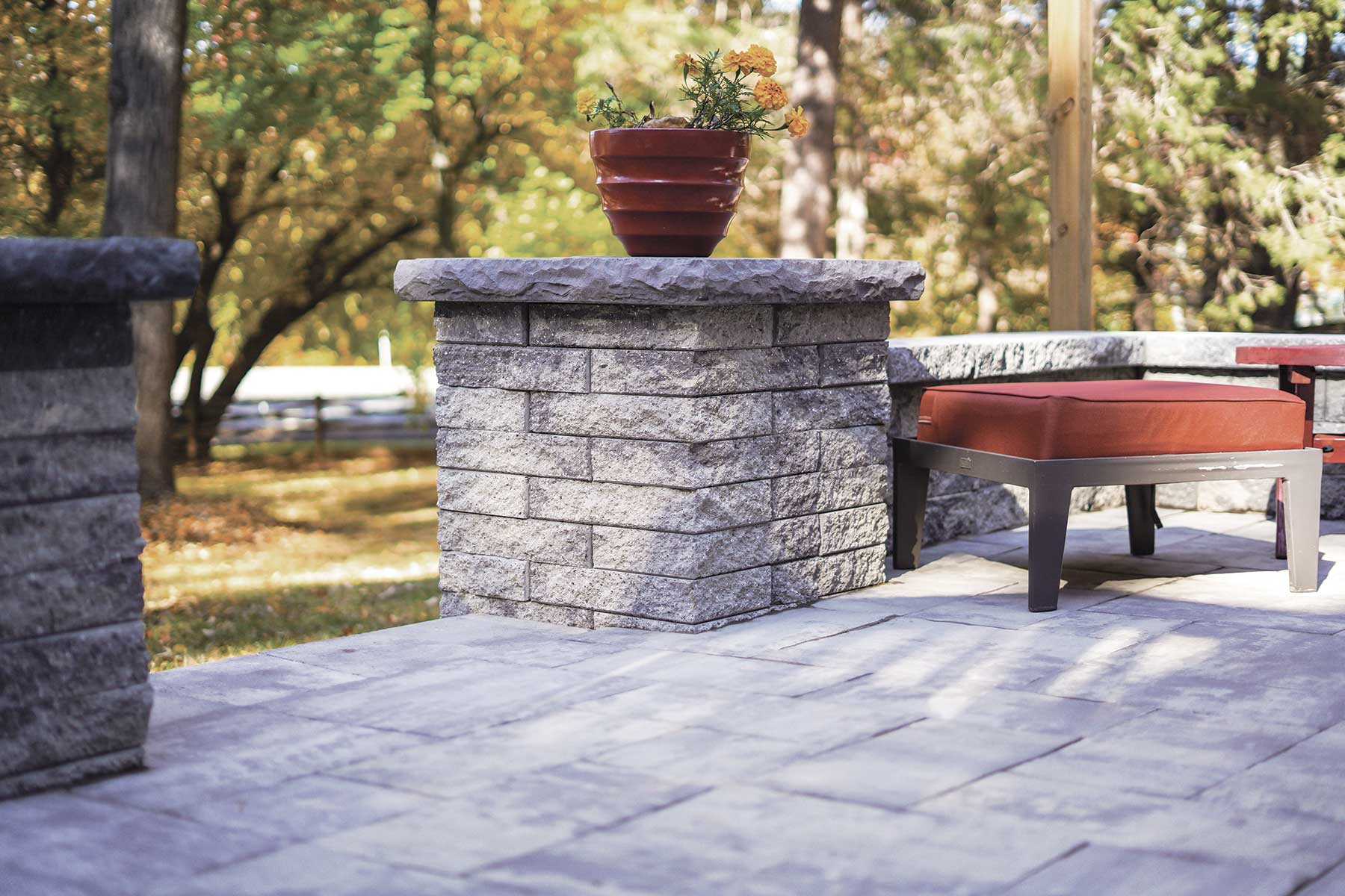 Stone pier caps topped with a planter beside a patio seat in a landscaped backyard setting.